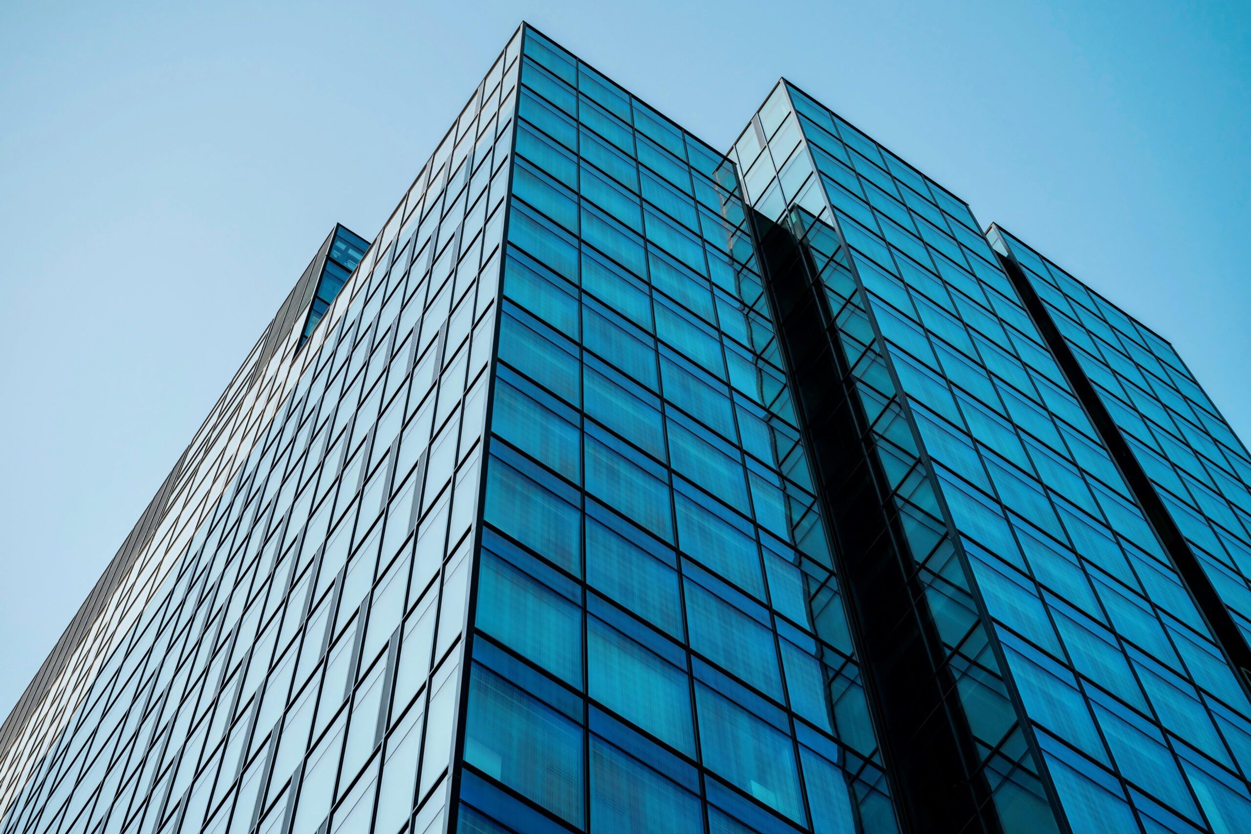 Low angle view of a modern skyscraper with a reflective glass facade reaching into a clear blue sky.